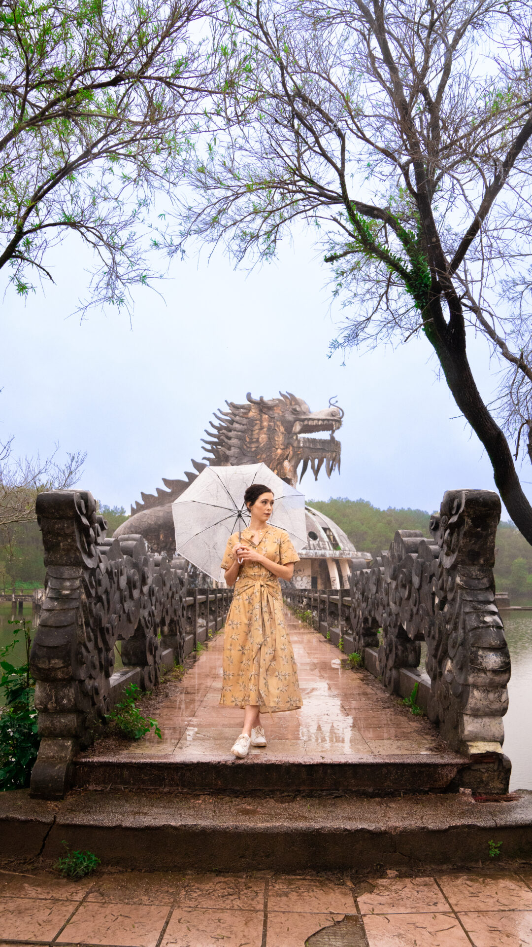 Travel Blogger Jordan Gassner holding an umbrella in the rain on a bridge leading to a dragon-shaped structure in Hue, Vietnam