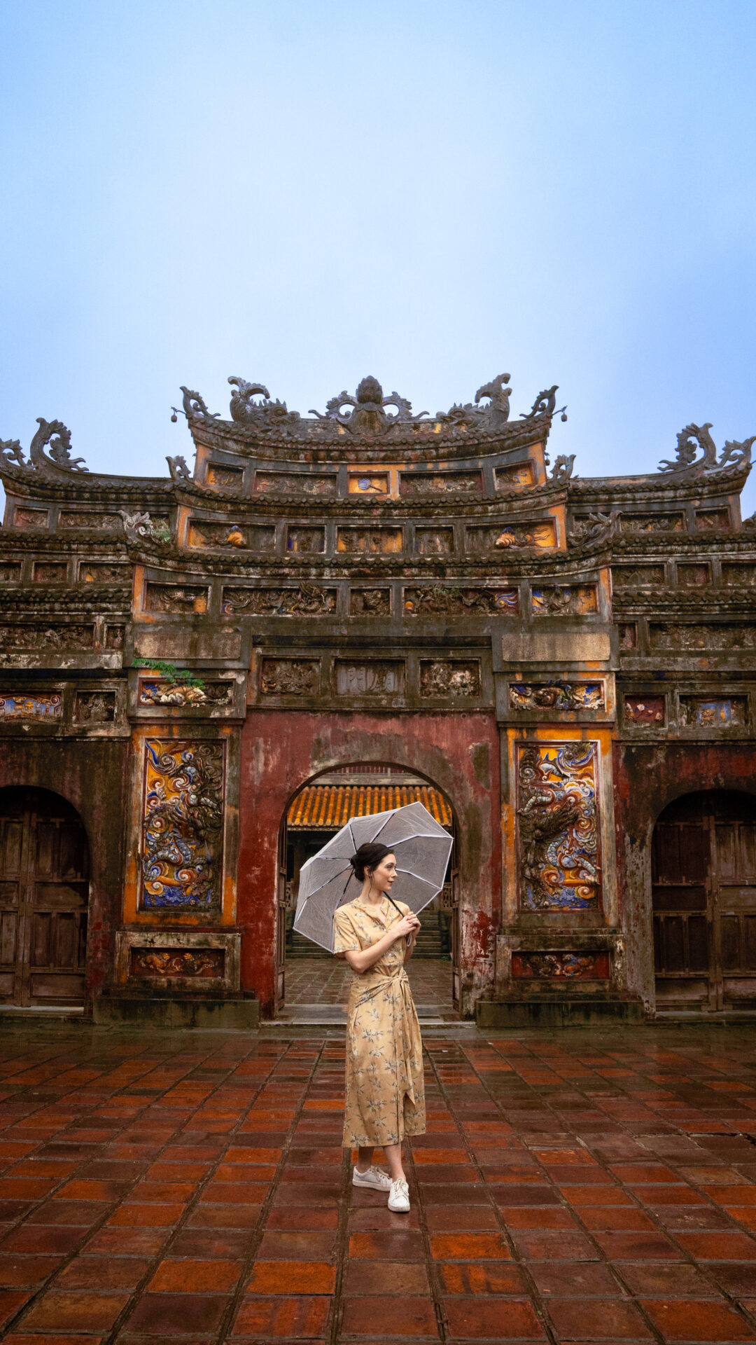 Travel Blogger Jordan Gassner holding an umbrella in the rain in front of a red, yellow and blue archway inside the Imperial Citadel of Hue in Vietnam