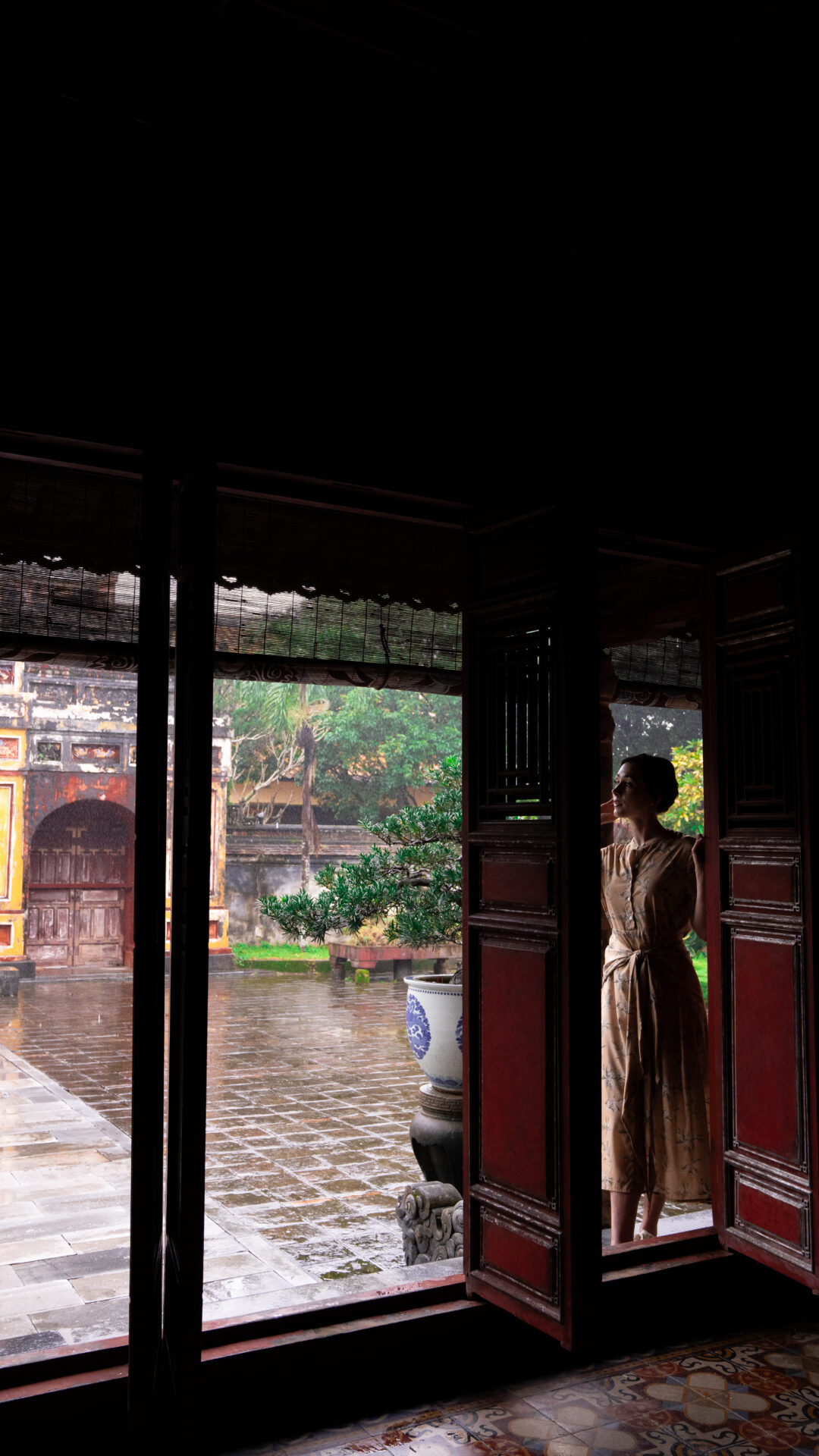 Travel Blogger Jordan Gassner looking over her shoulder from a red covered doorway inside one of the historic structures making up the Imperial City in Hue, Vietnam