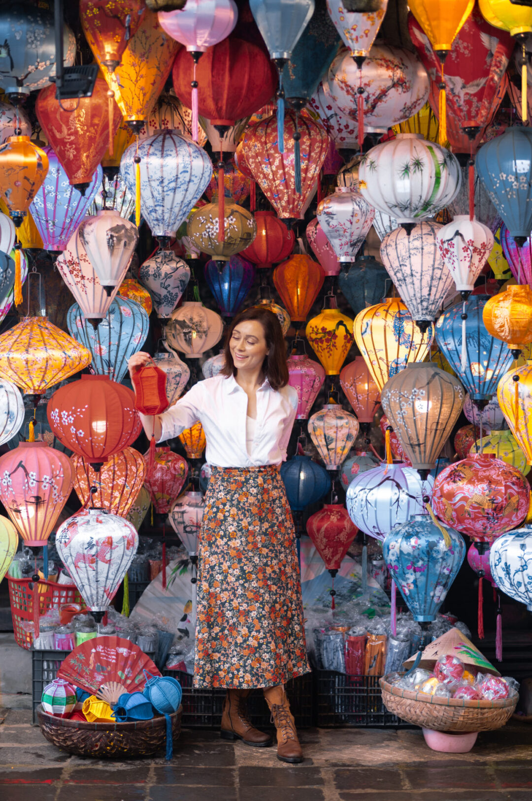Travel Blogger Jordan Gassner smiling while looking at a red lantern in her hand and standing inside a small lantern shop in Hoi An, Vietnam 