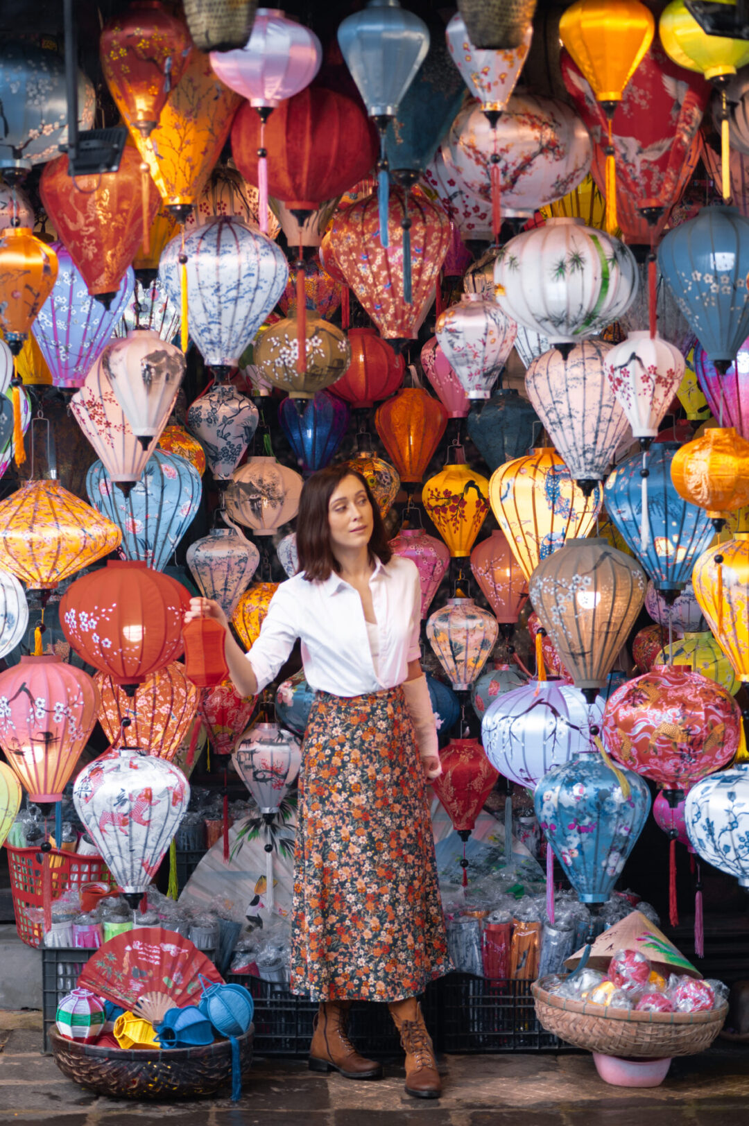 Travel Blogger Jordan Gassner looking around while holding a red lantern in her hand and standing inside a small lantern shop in Hoi An, Vietnam 