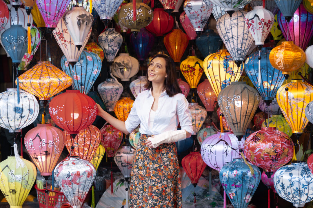 Travel Blogger smiling and looking up at the lanterns inside a small lantern shop in Hoi An, Vietnam 