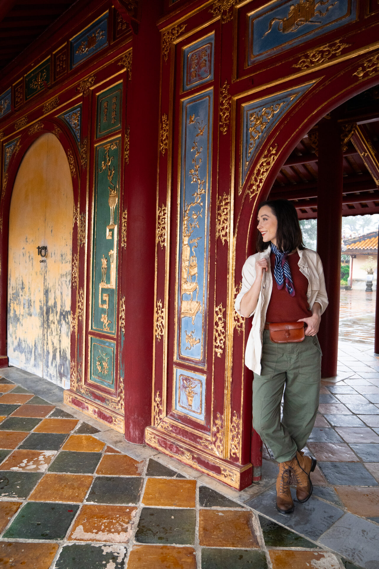 Travel Blogger Jordan Gassner leaning against a red, blue, green and gold doorway inside Minh Mang Tomb in Hue, Vietnam