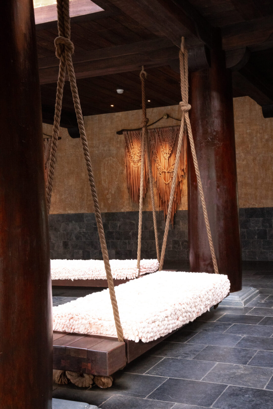 Large wooden swing benches hung up by thick ropes and covered with a soft, natural, textured fabric inside one of the common areas of Legacy Yen Tu Hotel in Vietnam