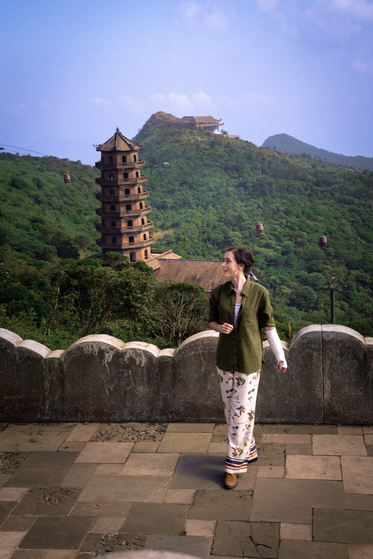 Travel Blogger Jordan Gassner smiling while standing near cloud-etched wall on top of Yen Tu Mountain and overlooking a chair lift and stupa in Northern Vietnam