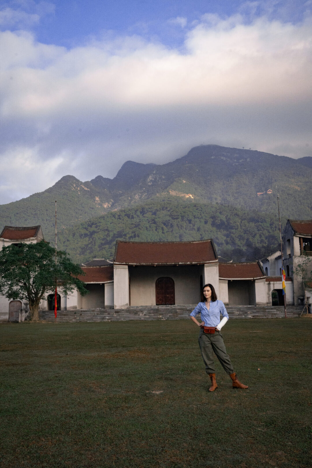 Travel Blogger Jordan Gassner standing in a green grassy riding field in front of the Yen Tu Mountain