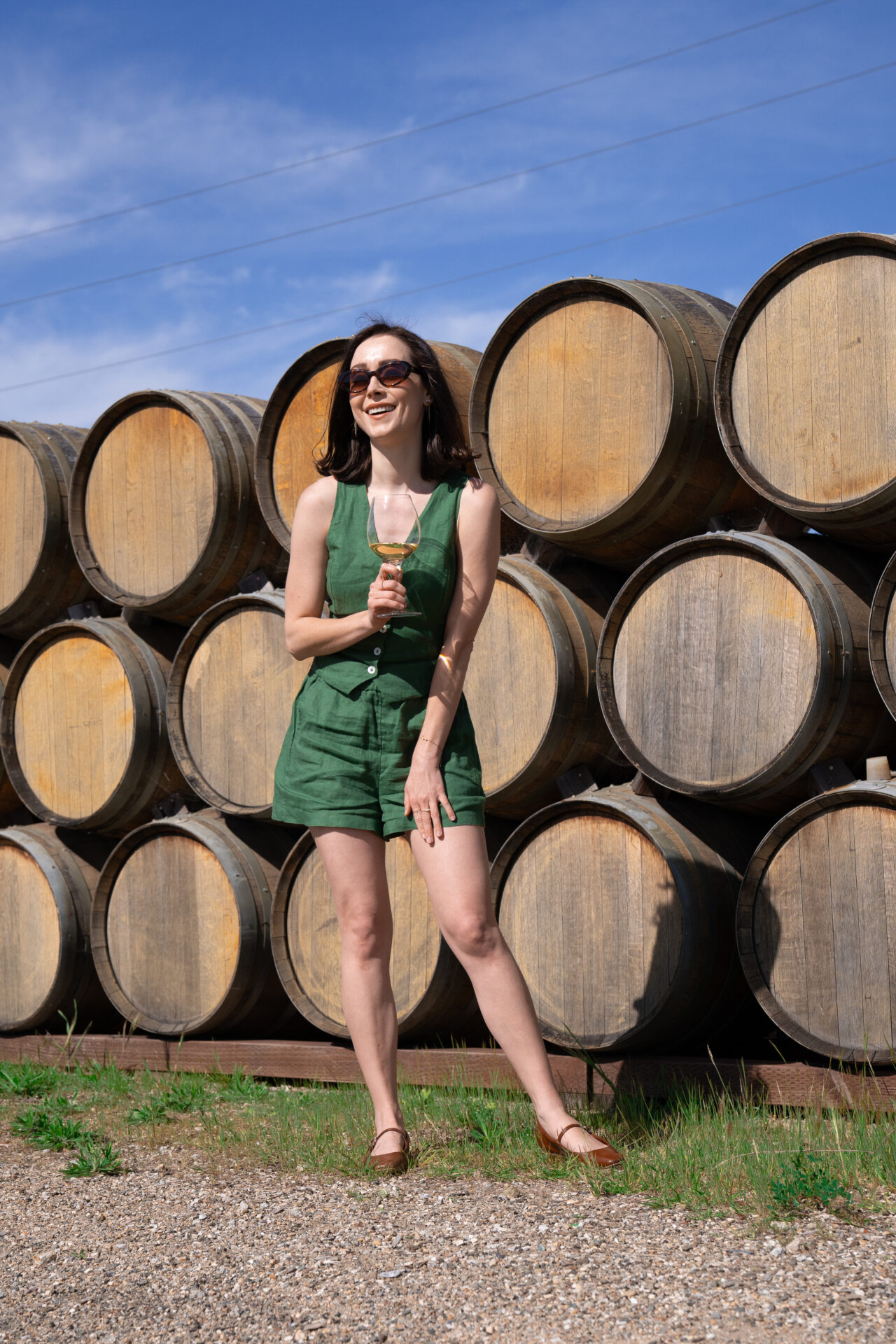 Travel Blogger Jordan Gassner holding a glass of wine and smiling in front of a row of wine barrels