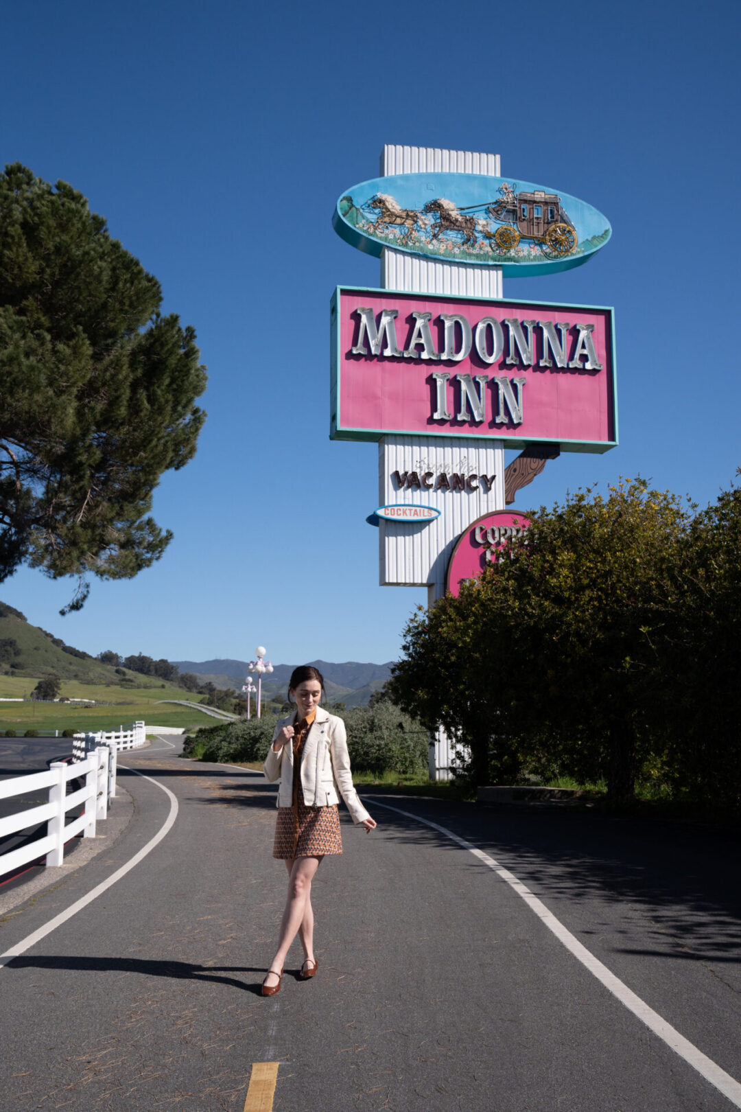 Travel Blogger Jordan Gassner walking along a bike path underneath the classic, pink Madonna Inn sign in San Luis Obispo, California