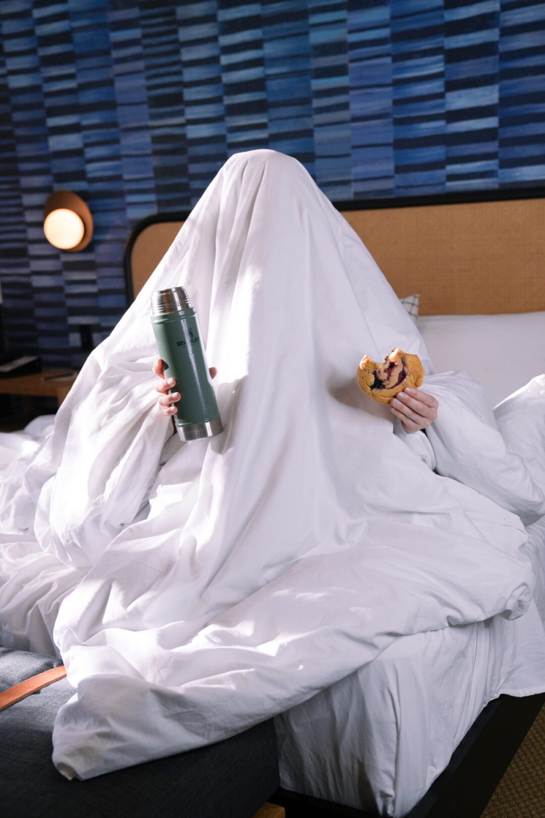 Travel Blogger Jordan Gassner sitting under a duvet holding up a scone and a thermos full of coffee, the breakfast offered at San Luis Creek Lodge