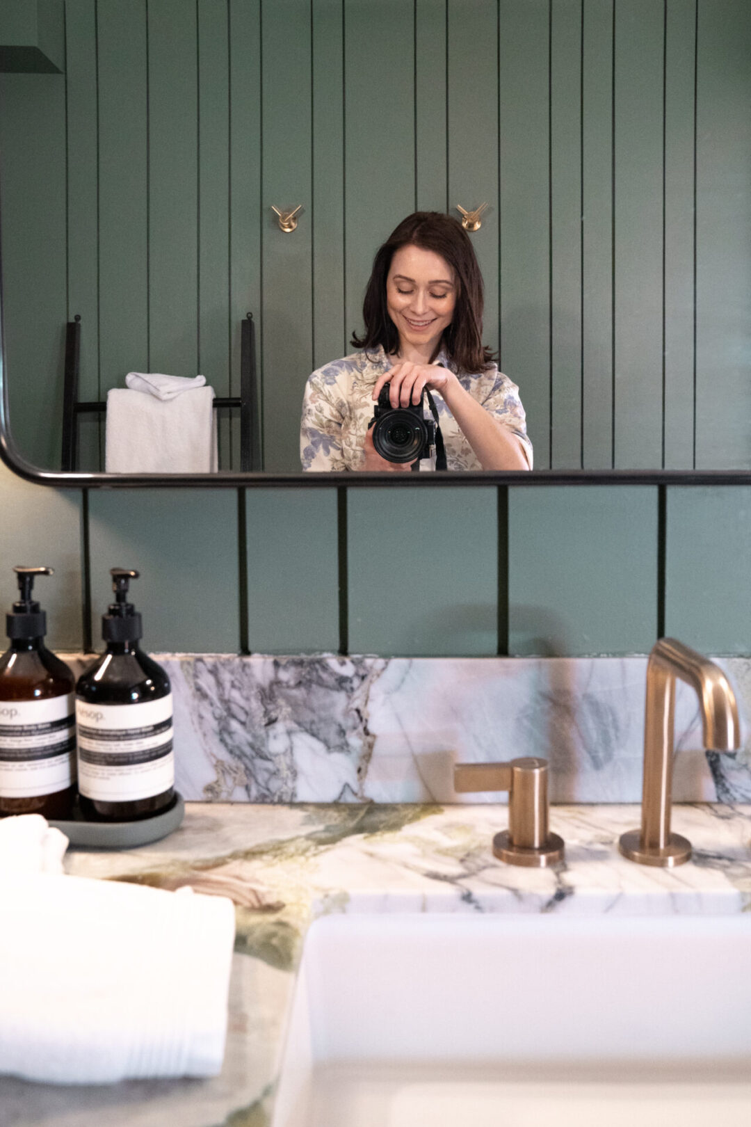 Travel Blogger Jordan Gassner smiling while taking a mirror selfie inside a beautiful green bathroom at San Luis Creek Lodge
