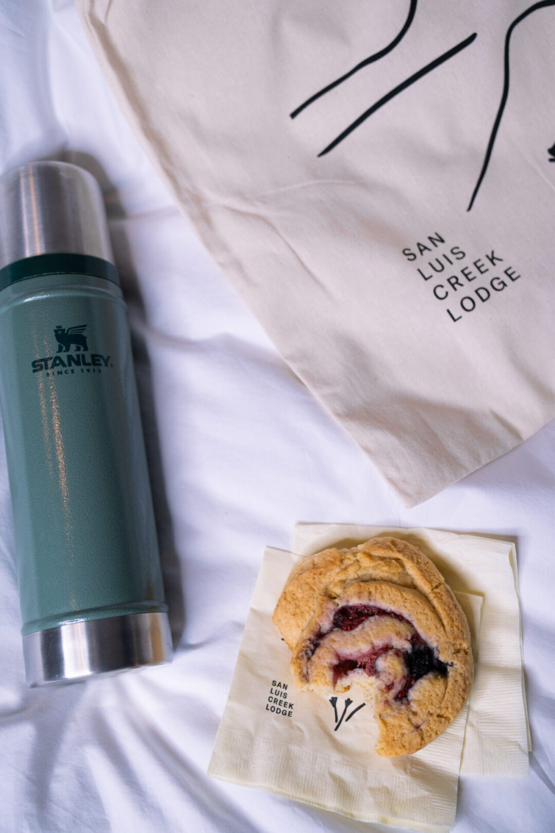 A scone and Stanley thermos full of coffee next to a canvas tote bag, the breakfast delivery from San Luis Creek Lodge in San Luis Obispo, California
