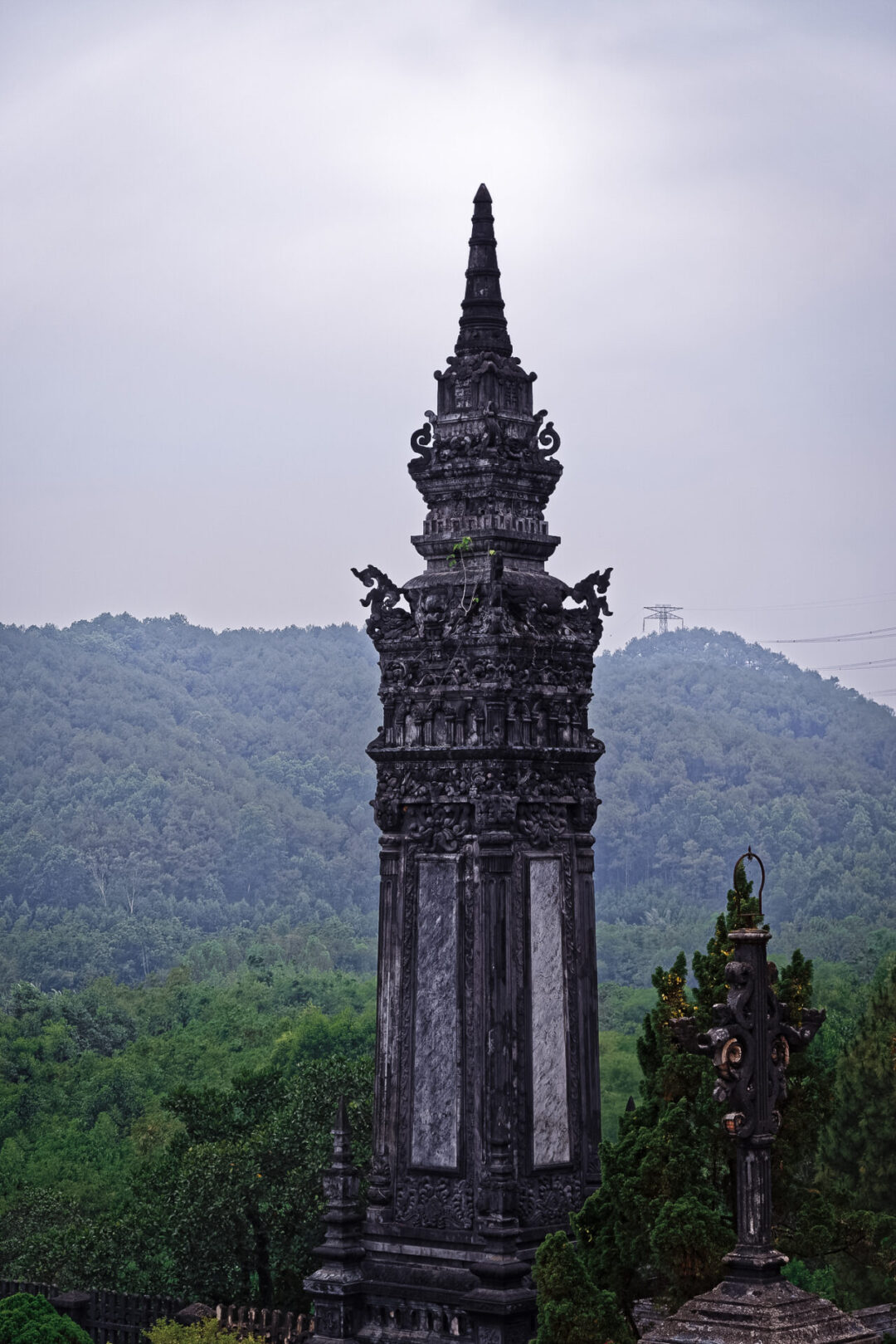 A black tower standing in front of green mountains at the Tomb of Khai Dinh in Hue, Vietnam