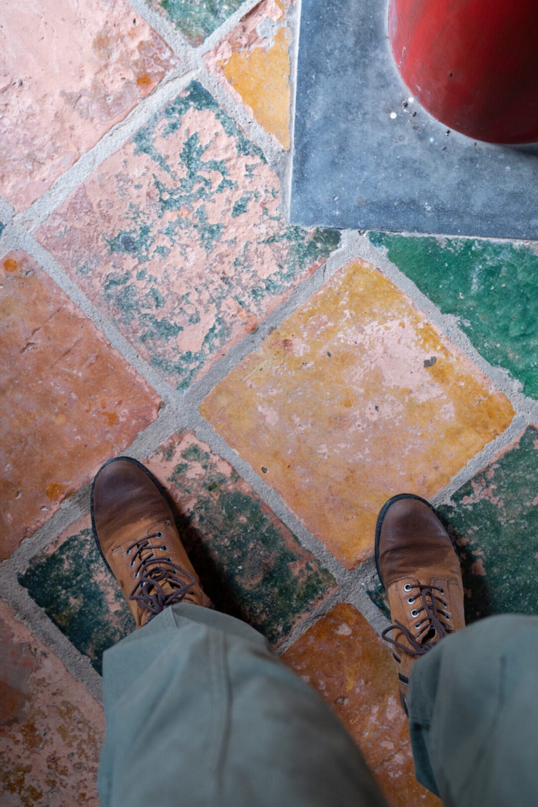 A first person's point of view of their brown boots on a set of green, yellow and coral colored tiles inside the the Tomb of Minh Mang in Hue, Vietnam