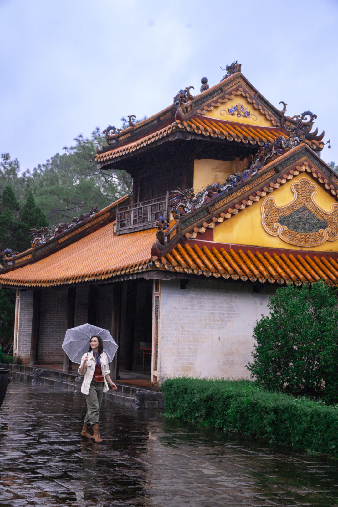 Travel Blogger Jordan Gassner walking with an umbrella in hand near one of the structures inside the Tomb of Tu Duc during the rainy season in Hue, Vietnam 
