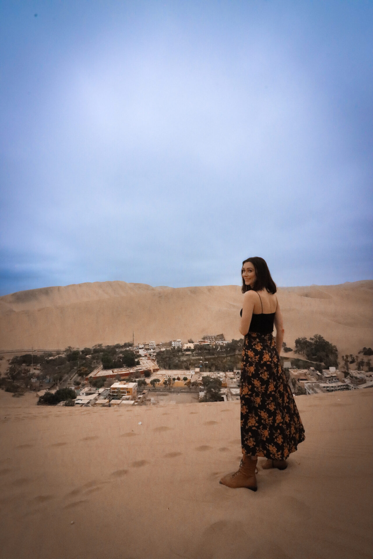Travel Blogger Jordan Gassner smiling atop a sand dune over Huacachina, Peru