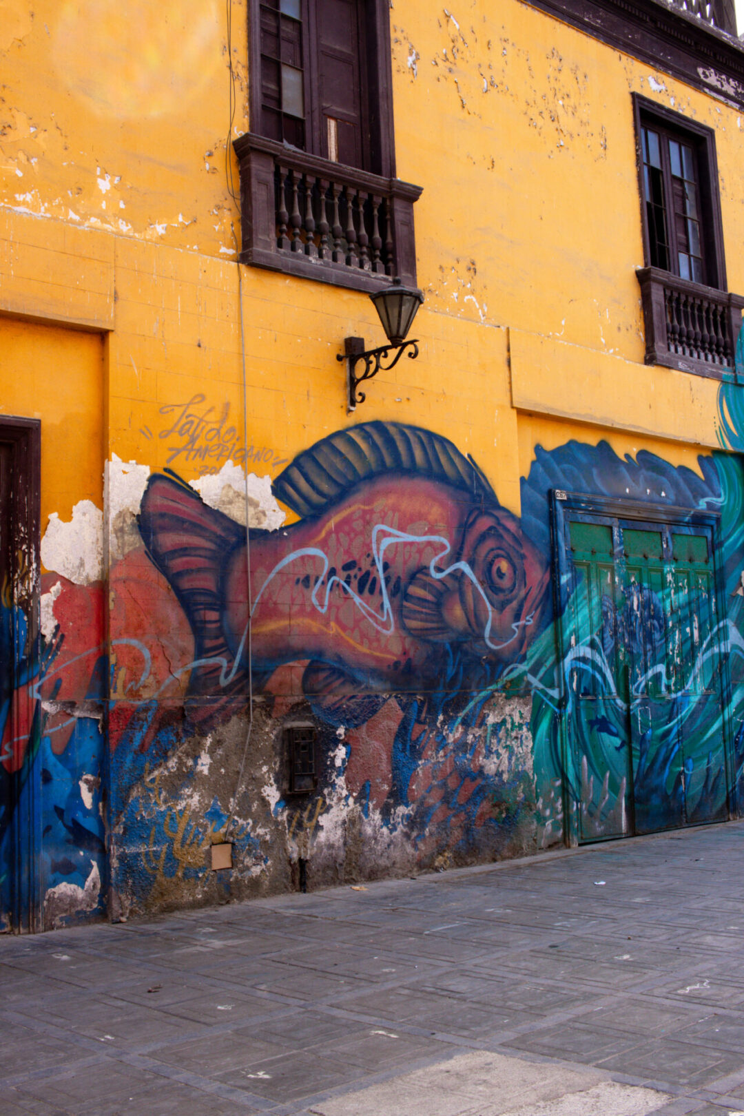A colorful fish and ocean themed piece of graffiti set against a yellow building in Callao, Peru