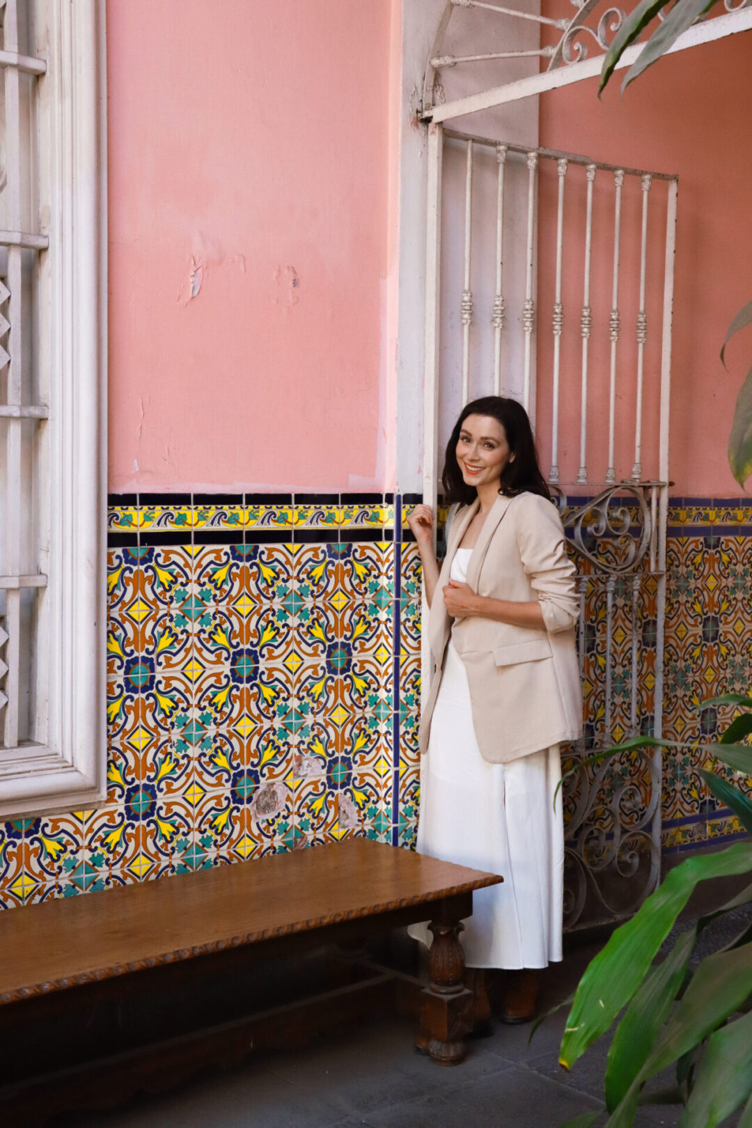 Travel Blogger Jordan Gassner standing next to a white wrought-iron gate an coral-painted wall decorated with turquoise, blue and yellow tiles in Lima, Peru
