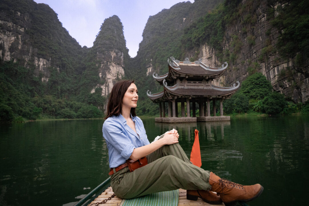 Travel Blogger Jordan Gassner sitting on a boat in front of a floating pagoda inside Trang An Landscape Complex in Ninh Binh, Vietnam