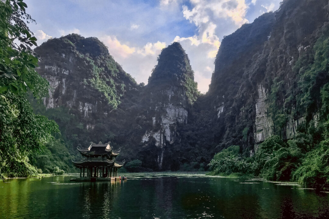 A double-roofed water pagoda dwarfed by the large surrounding limestone karsts in Trang An in Vietnam