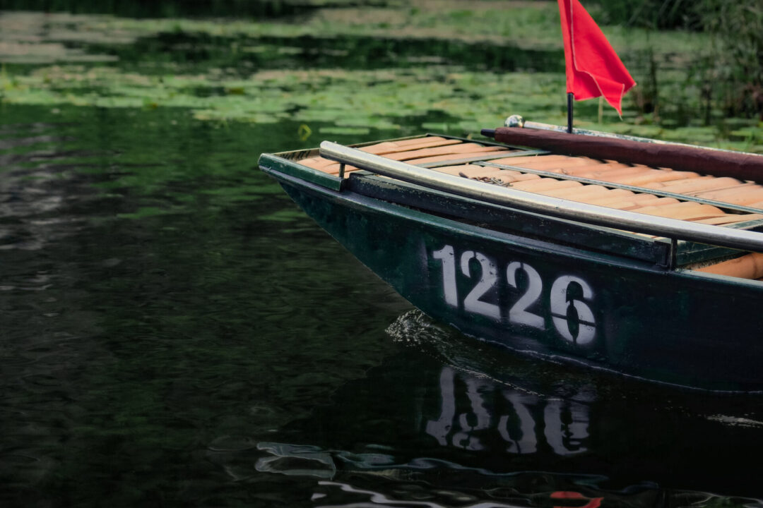A green sampan boat with a red flag and the white painted boat number, "1226", painted on its side