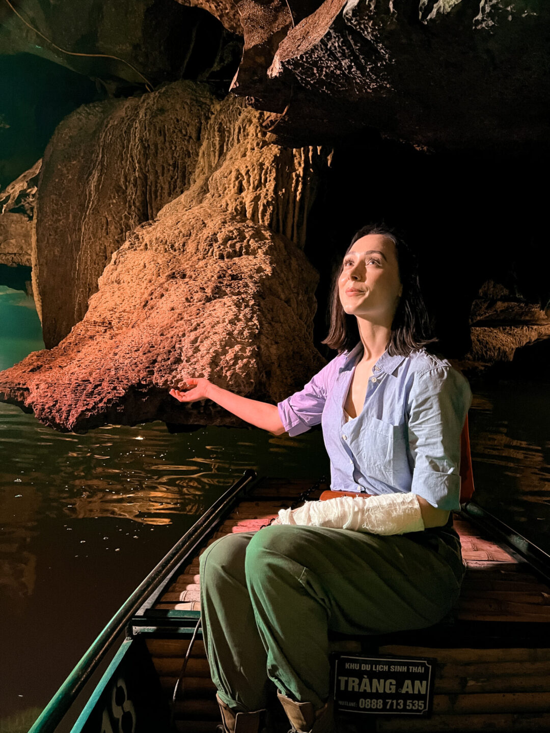 Travel Blogger Jordan Gassner reaching out from a sampan boat to catch water about to drip from one of the stalactites inside a cave at Trang An, Vietnam

