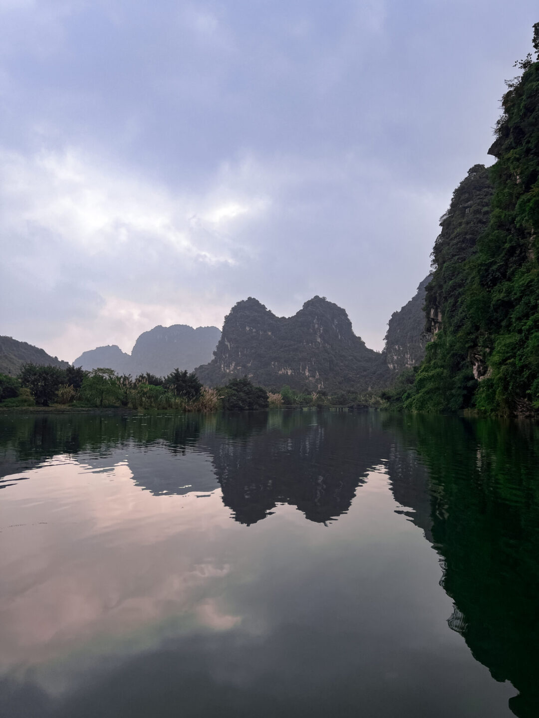 A double crowned limestone karst perfectly reflected in the surrounding water near sunrise at Trang An Landscape Complex in Vietnam