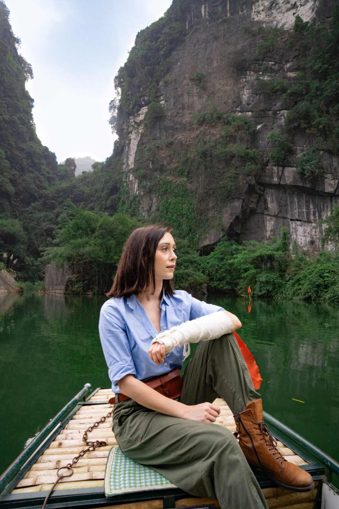 Travel Blogger Jordan Gassner sitting on the edge of a traditional sampan boat in Trang An Landscape Complex in Ninh Binh, Vietnam