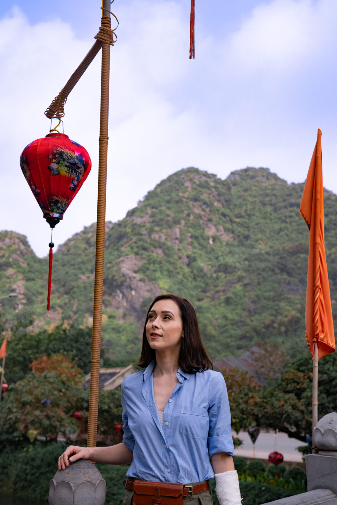 Travel Blogger Jordan Gassner standing on a bridge and looking at the colorful flags and lanterns adorning it in Ninh Binh, Vietnam