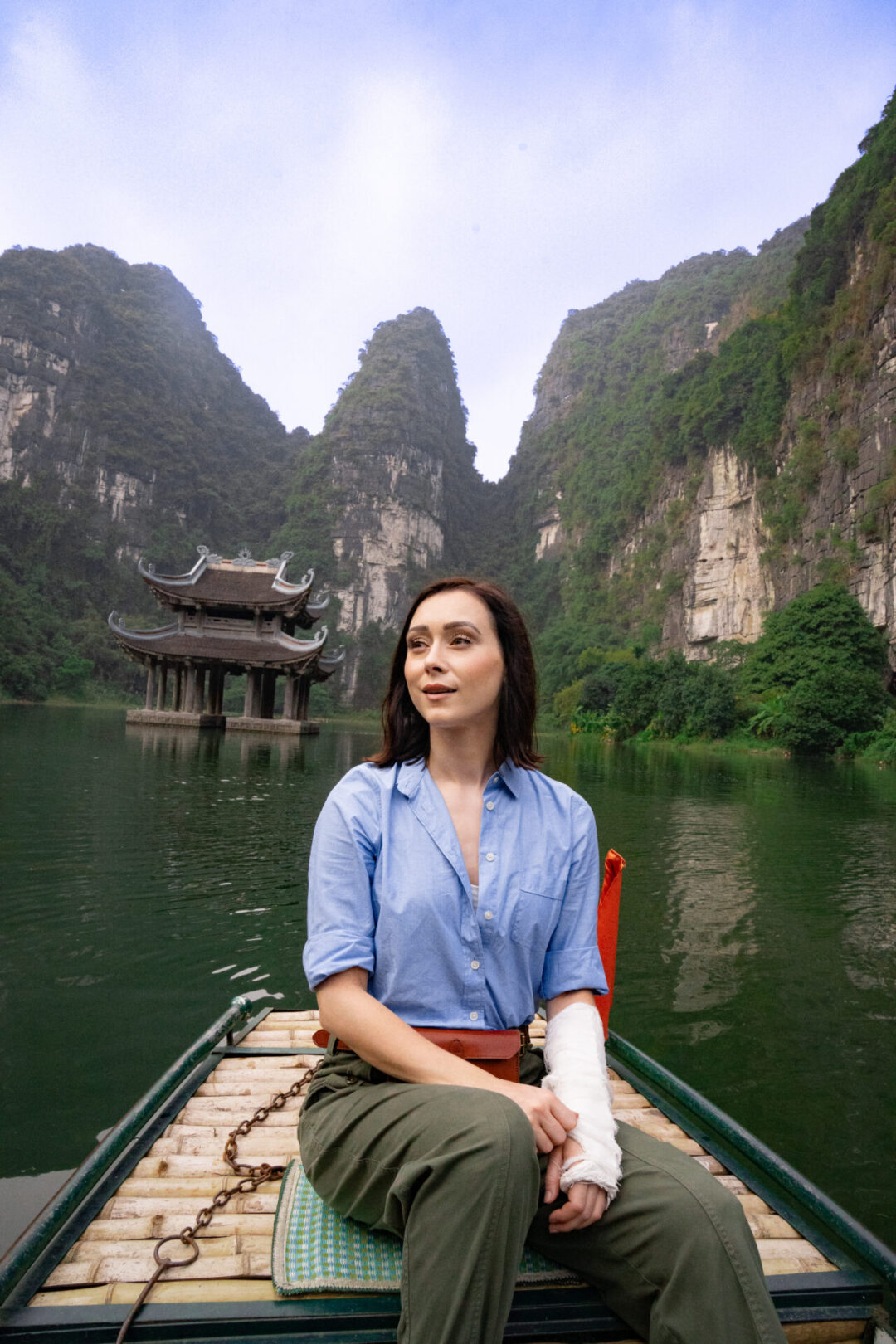 Travel Blogger Jordan Gassner floating near a double-roofed water pagoda from a traditional sampan boat in Trang An Landscape Complex in Ninh Binh, Vietnam