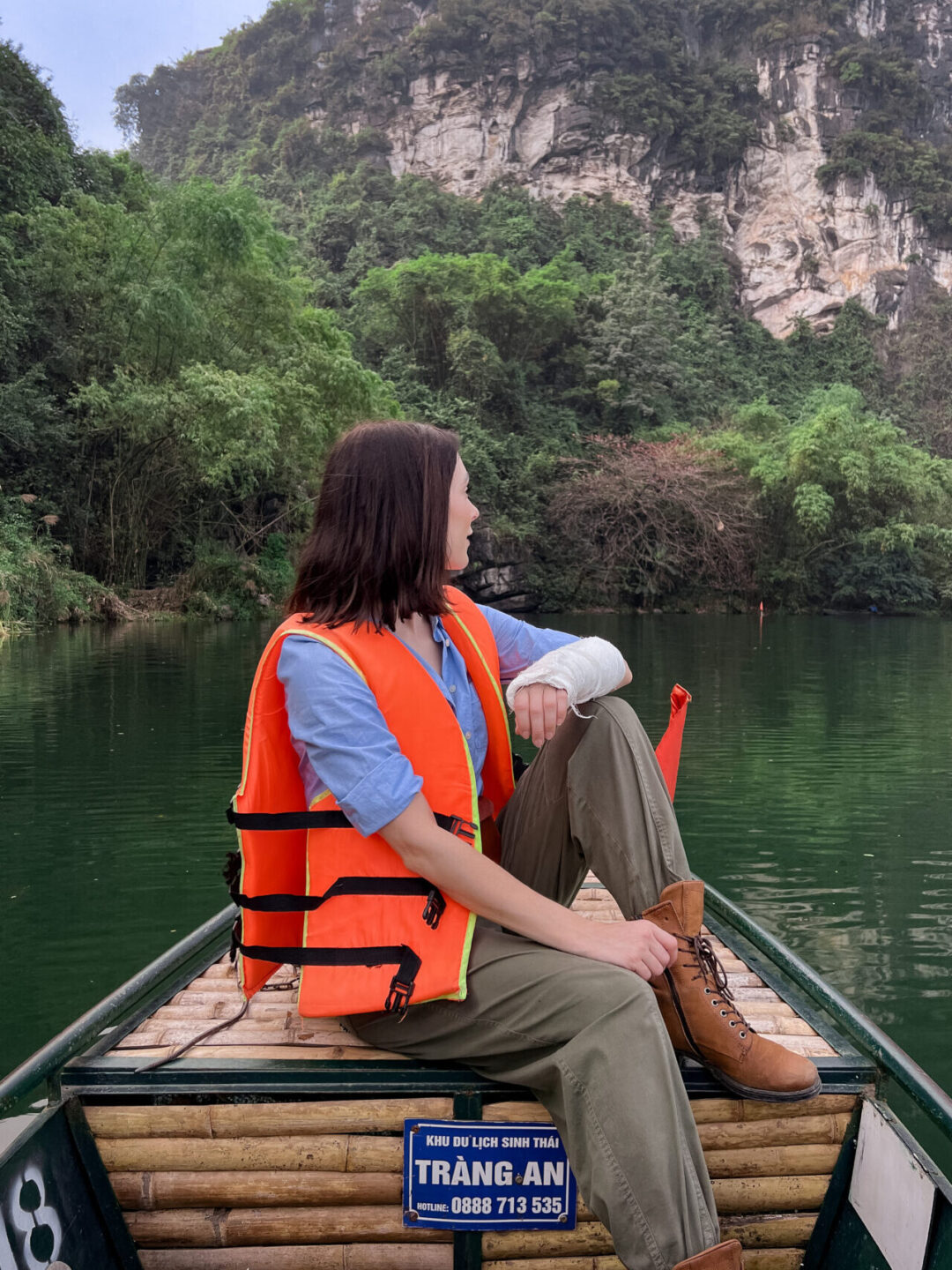 Travel Blogger Jordan Gassner sitting looking behind her while wearing an inflatable life vest inside a traditional sampan boat in Trang An Landscape Complex in Ninh Binh, Vietnam