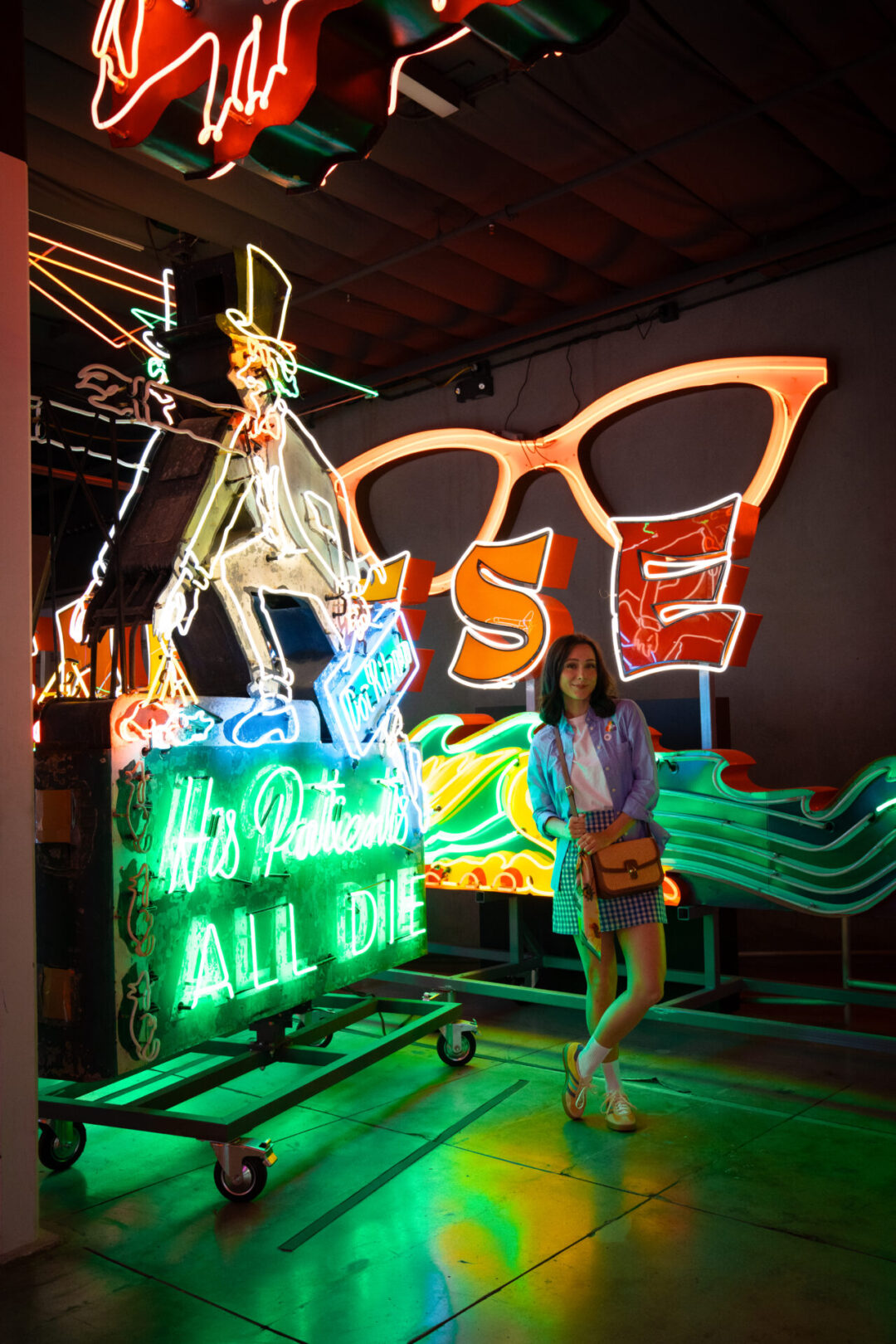 Travel Blogger Jordan Gassner standing and smiling in front of a few bright neon signs at the Museum of Neon Art in Los Angeles, California