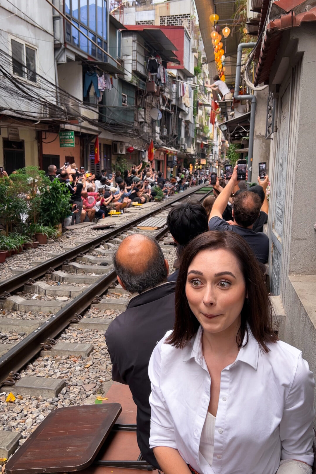 Travel Blogger Jordan Gassner smiling anxiously while sitting along Hanoi's Train Street as a train approaches