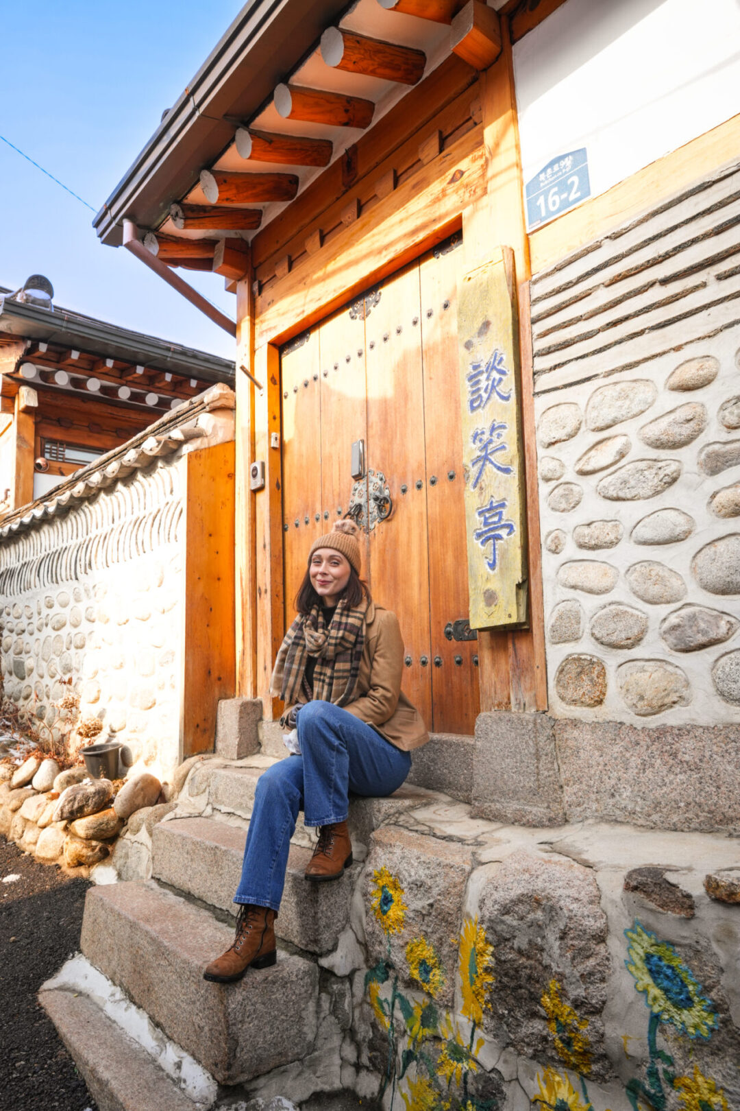 Travel Blogger Jordan Gassner sitting near a gate decorated with colorful floral paintings inside Bukchon Hanok Village in Seoul, South Korea