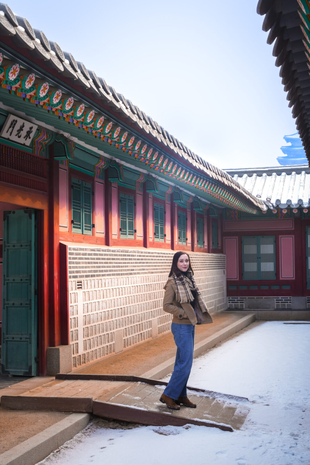 Travel Blogger Jordan Gassner wrapping her hands in her coat while exploring Jagyeongjeon Hall on a snowy day inside Gyeongbokgung Palace
