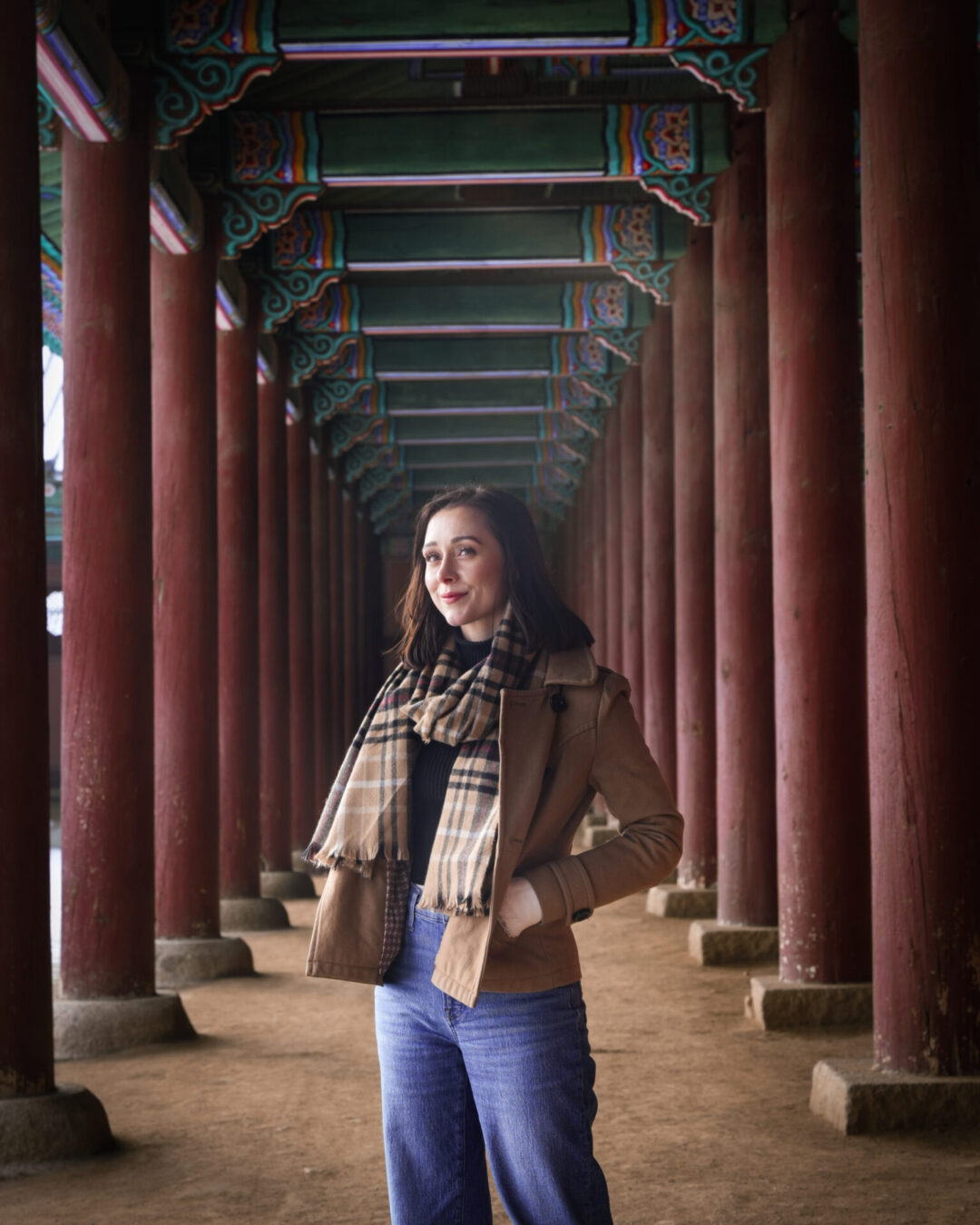 Travel Blogger Jordan Gassner standing underneath the red painted colonnade surrounding Geunjeongjeon Hall inside Gyeongbokgung Palace in Seoul