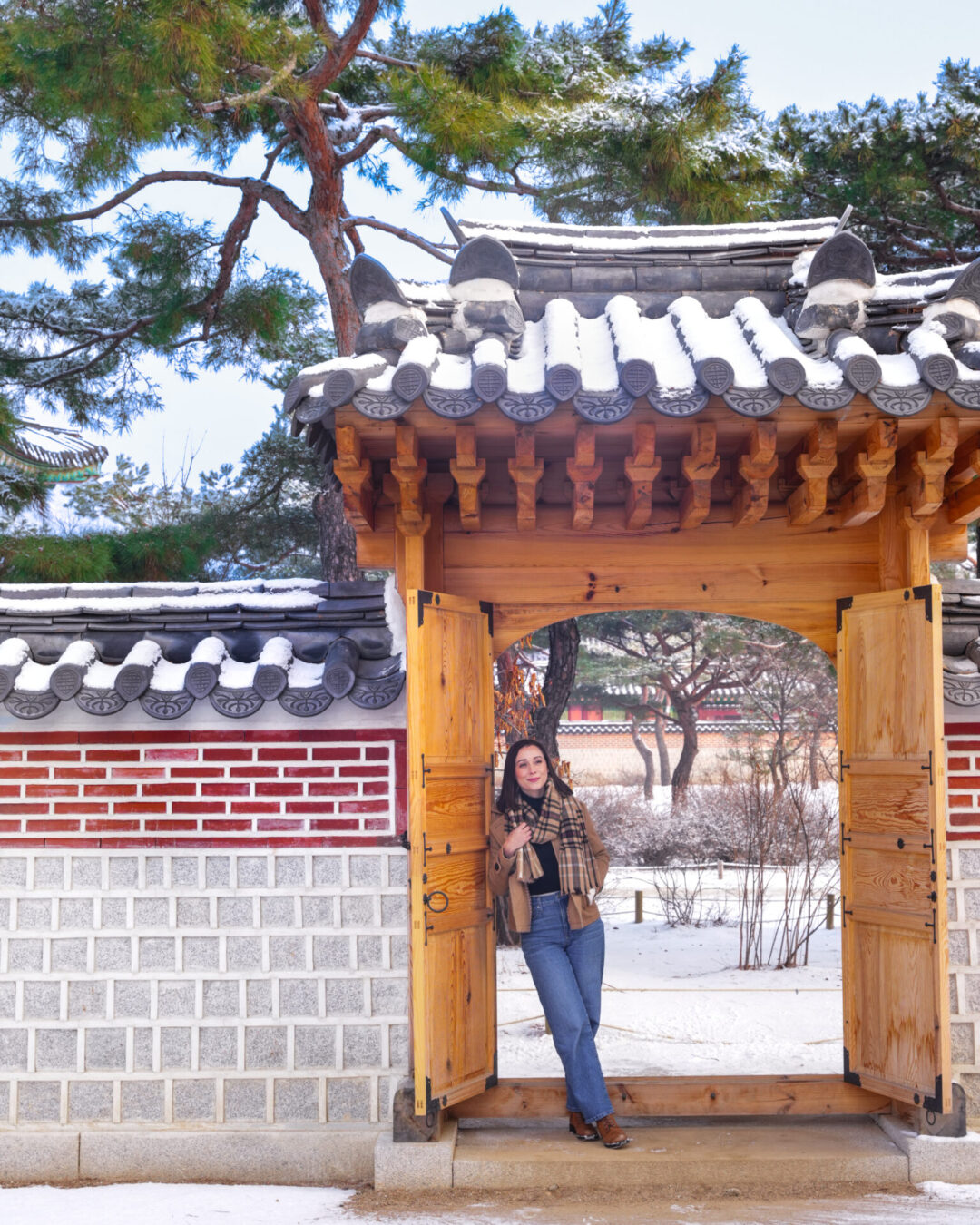 Travel Blogger Jordan Gassner leaning against a natural wood gate in between Geonchunmun Gate and Gyejodang Hall inside Gyeongbokgung Palace in Seoul