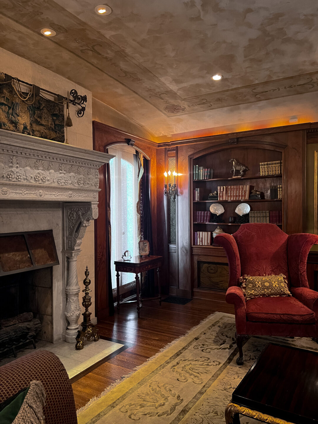 A large stone fireplace and velvet arm chair sitting in the decadent living room inside the Wrigley Mansion in Pasadena, California