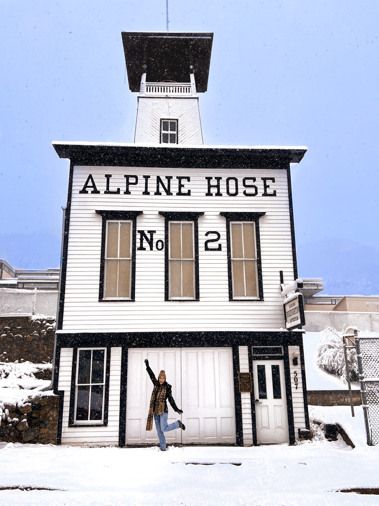 Travel Blogger Jordan Gassner throwing her arms and legs up while standing in front of the Alpine Hose No. 2 Firefighting station in Georgetown, Colorado