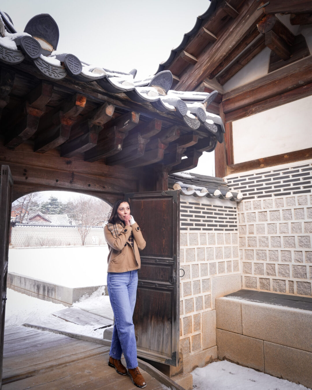 Travel Blogger Jordan Gassner blowing warm air into her hands at a gate on a snowy day in Seoul, South Korea