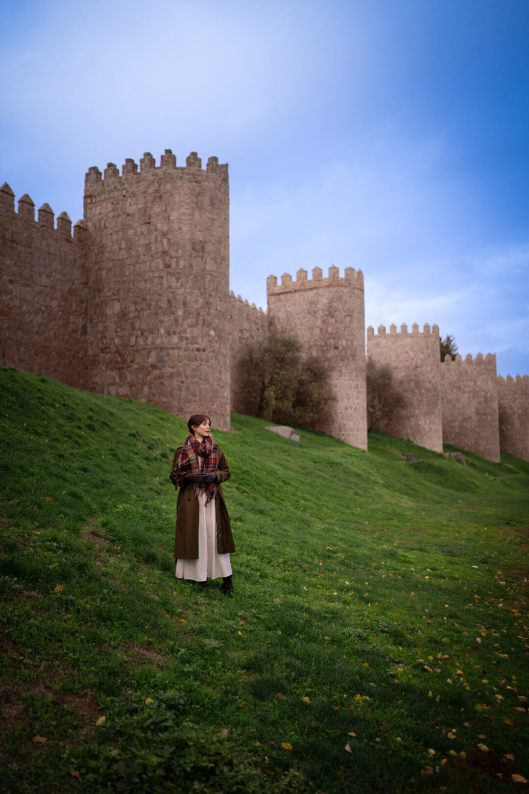 Travel Blogger Jordan Gassner standing on top of a green hill in front of the medieval walls of Avila in Central Spain