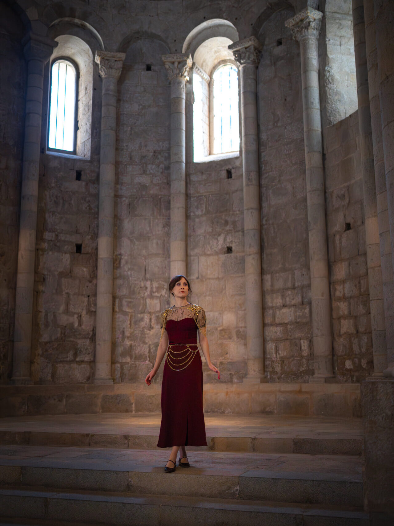 Travel Blogger Jordan Gassner wearing a medieval inspired dress and gold fishmail inside Sant Pere de Galligants, a Game of Thrones filming location in Spain