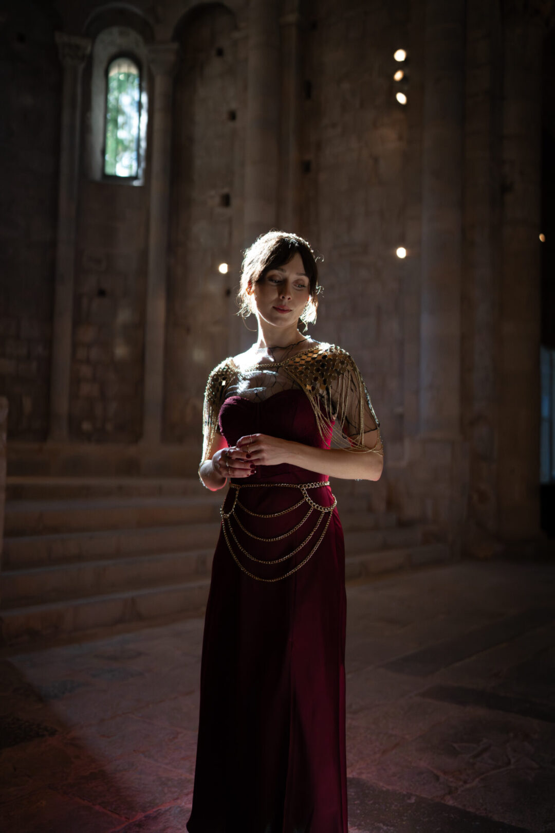 Travel Blogger Jordan Gassner wearing a medieval inspired dress and gold fishmail inside Sant Pere de Galligants, a Game of Thrones filming location in Spain