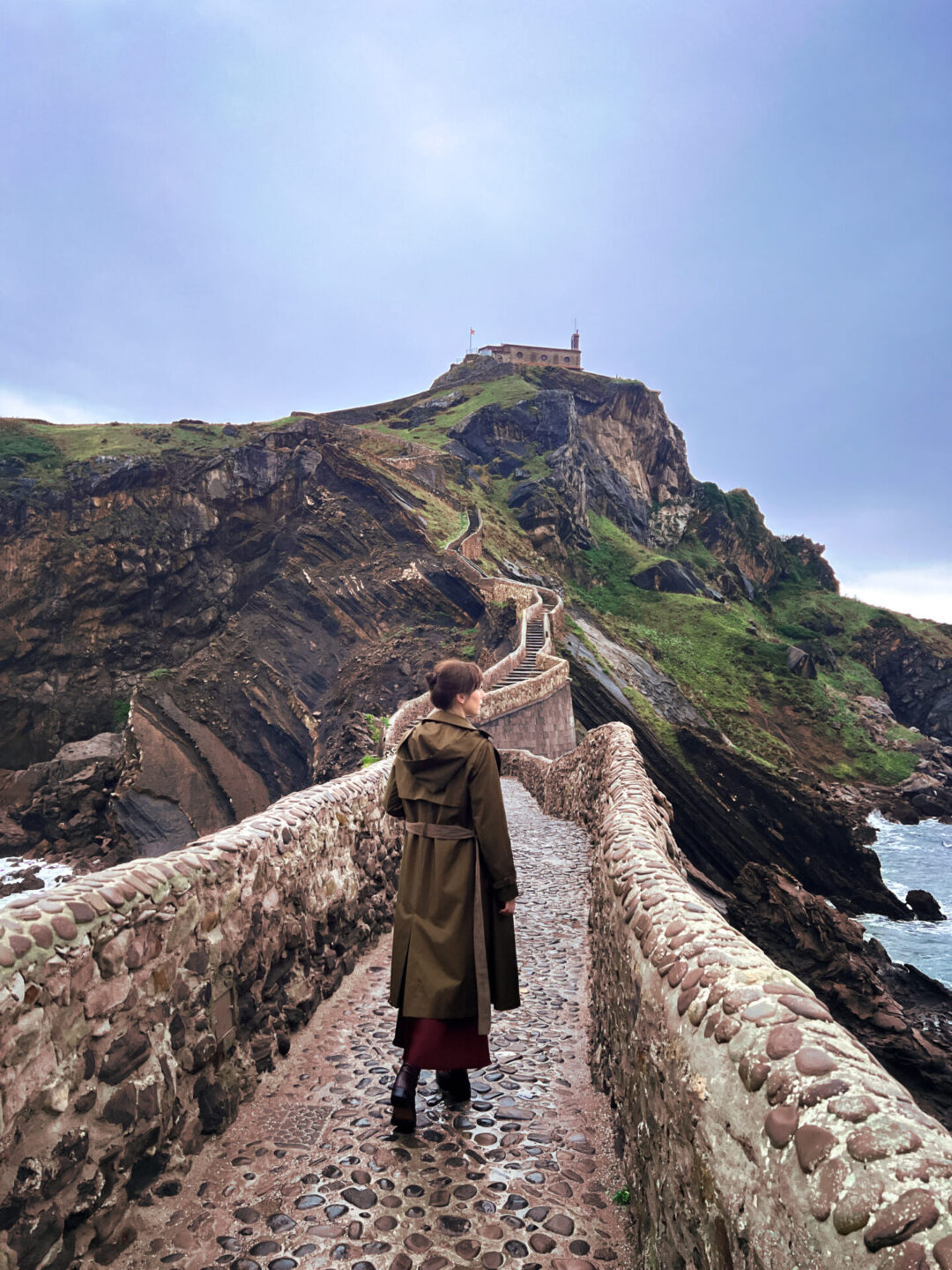 Travel Blogger Jordan Gassner walking along the pathway before the stairs along the stone stairway to San Juan de Gaztelugatxe in Spain