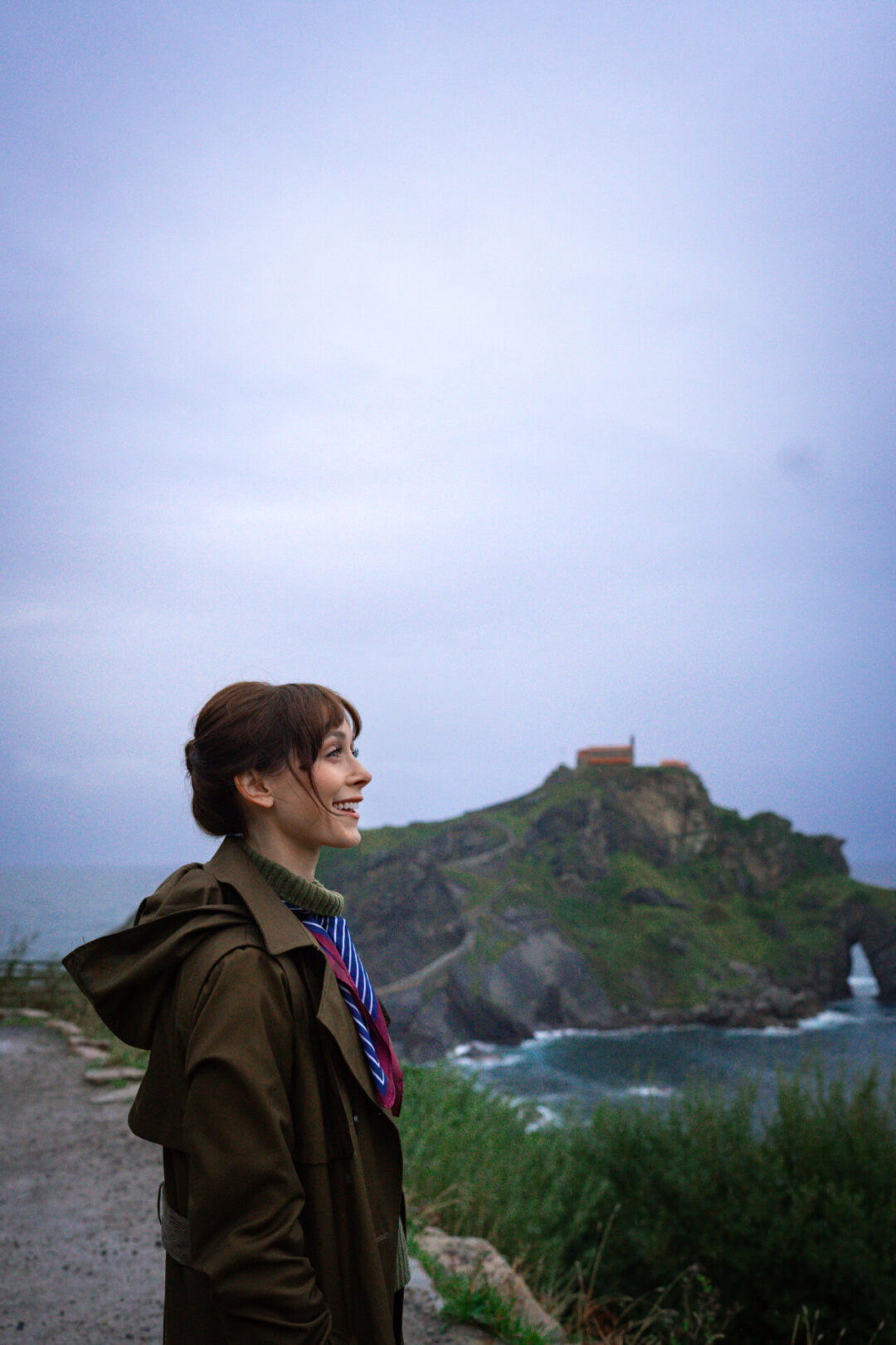 Travel Blogger Jordan Gassner smiling while looking out on a service road leading up to San Juan de Gaztelugatxe in Spain