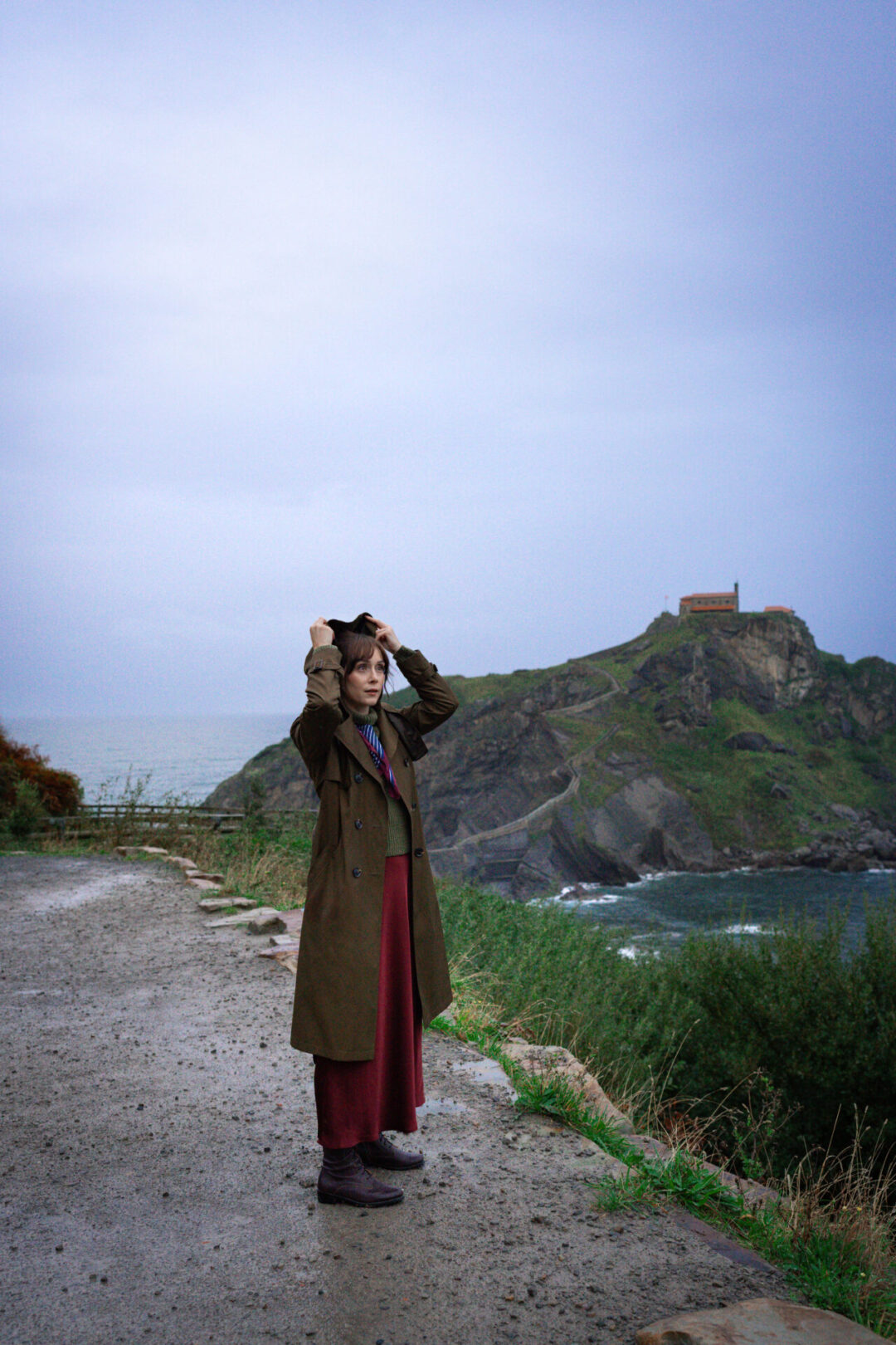Visiting San Juan De Gaztelugatxe - Travel Blogger Jordan Gassner putting a hood over her hair in the rain near San Juan de Gaztelugatxe