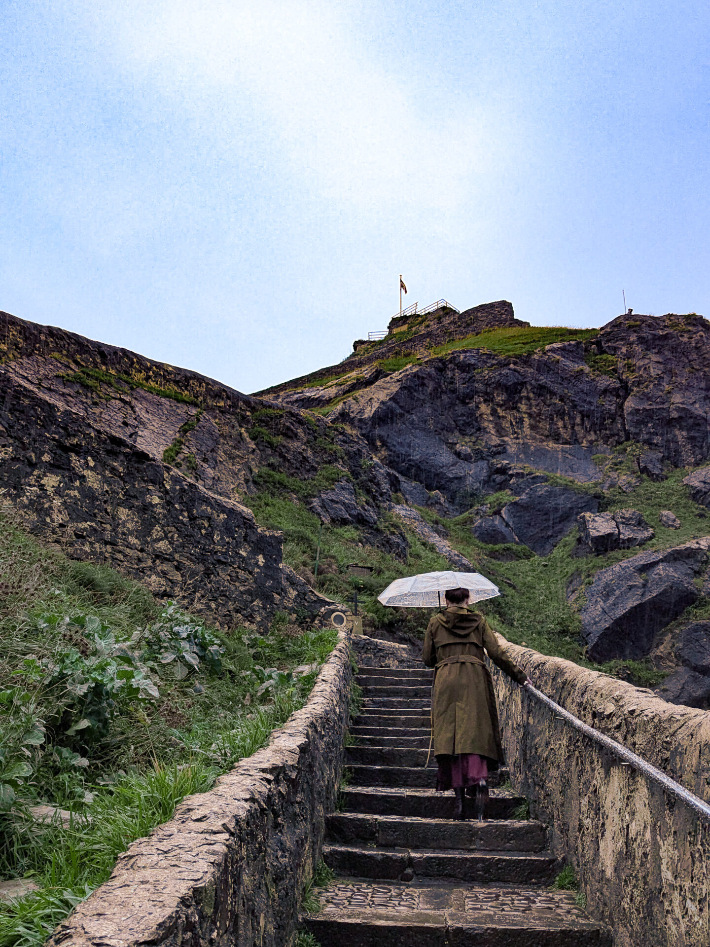 Travel Blogger Jordan Gassner climbing up the stairs with an umbrella to the San Juan de Gaztelugatxe summit in Spain