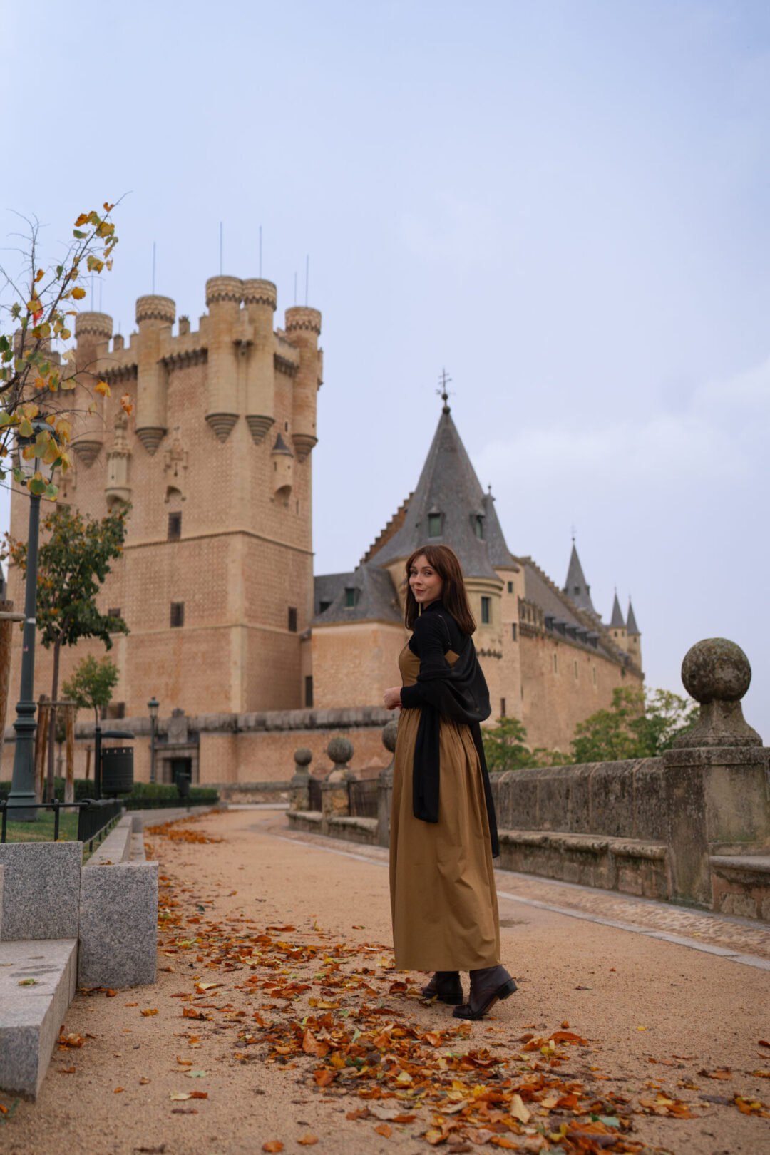 Travel Blogger Jordan Gassner wearing a long dress and looking over her shoulder while walking toward the Segovia Alcazar in Central Spain