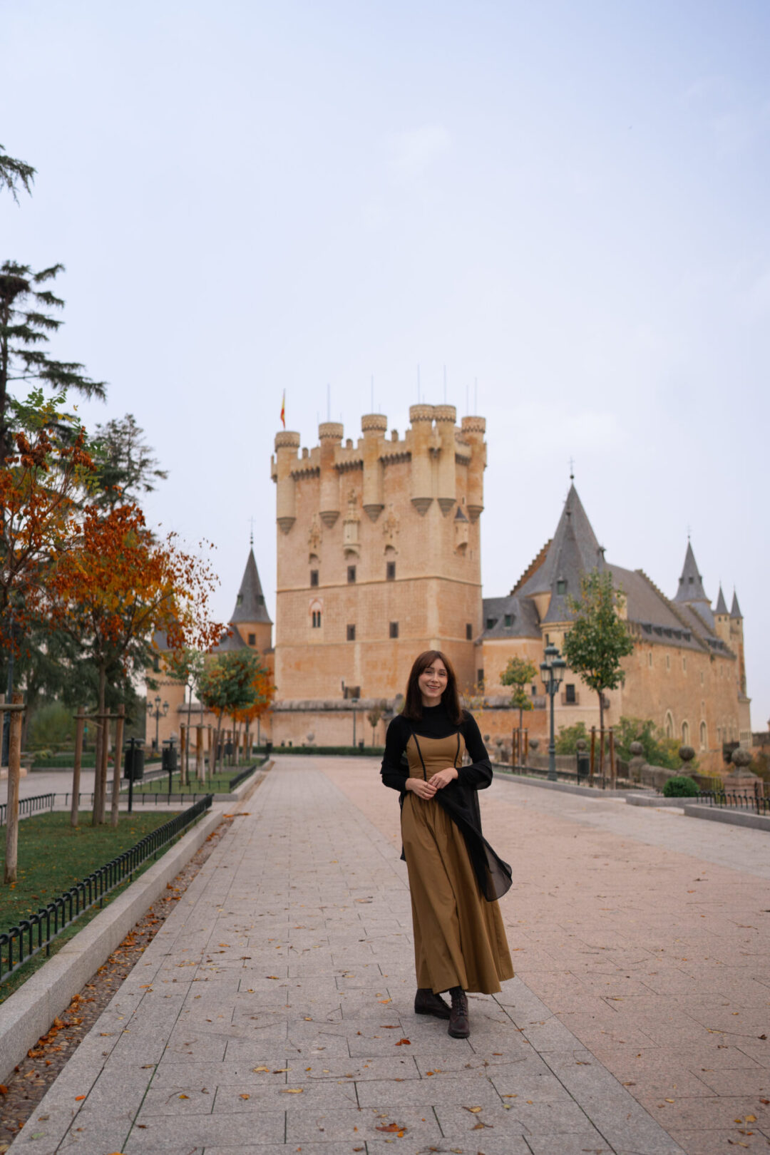Travel Blogger Jordan Gassner smiling while walking along a walkway in front of Segovia's Alcazar in Central Spain