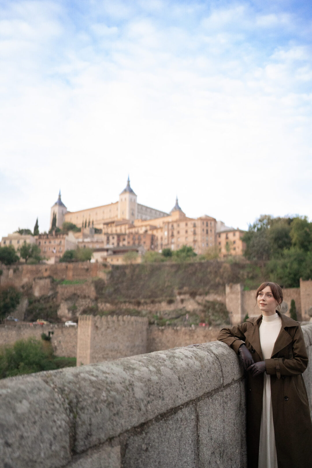 Travel Blogger Jordan Gassner leaning against the railing of Alcantara Bridge with the Alcazar in the background at sunrise in Toledo, Spain