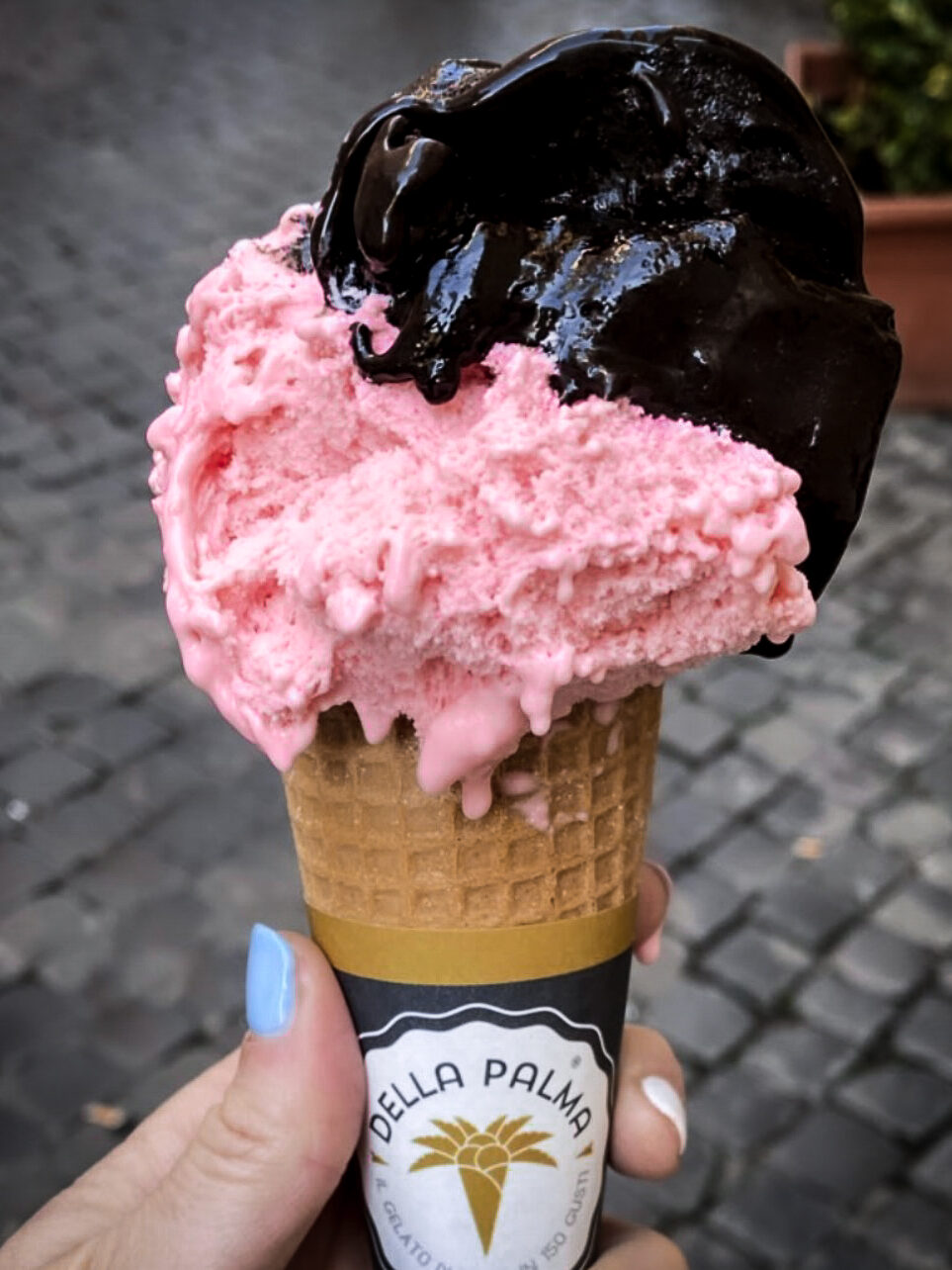 A woman with colorful nail polish holding up an ice cream cone from Della Palma Gelateria in Rome, Italy
